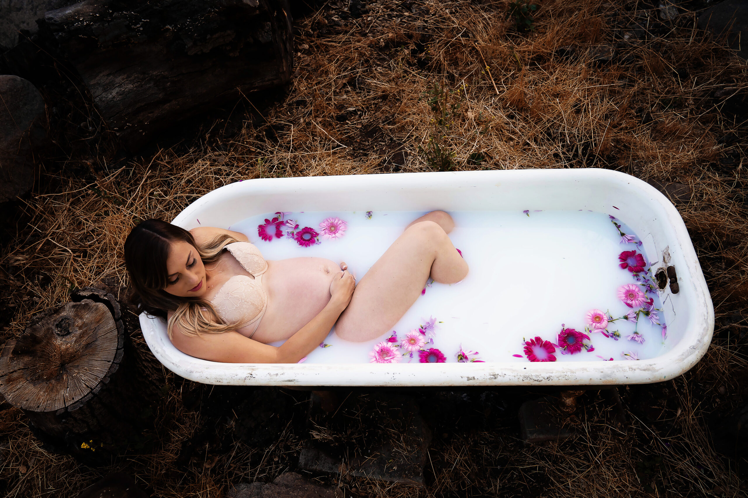 Woman lays in outdoor bathtub for boudoir maternity photos also known as a milk bath.