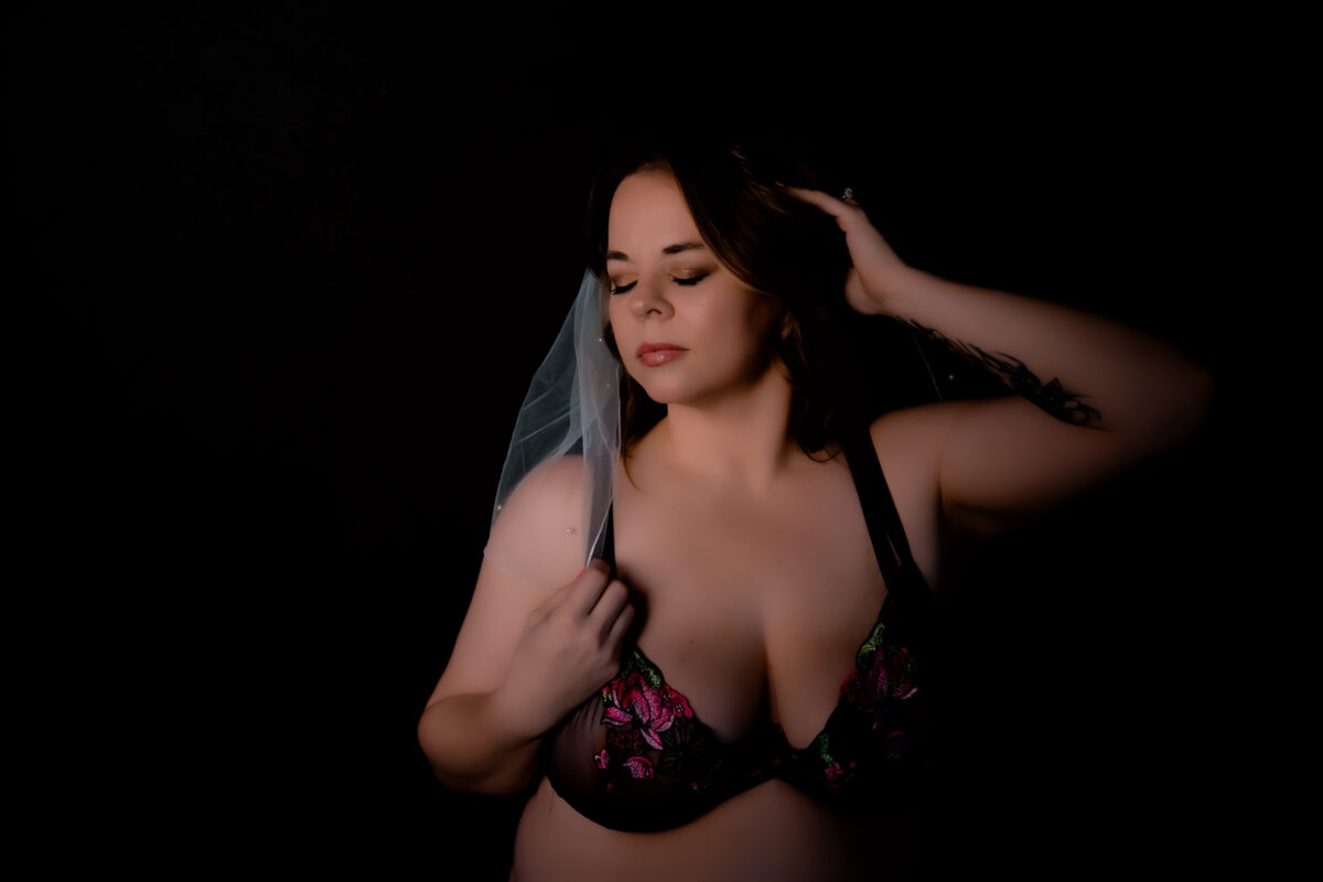 A bride wearing black lingerie and a white veil poses for bridal boudoir photos, near St.Louis, creating the perfect wedding day gift for her husband.