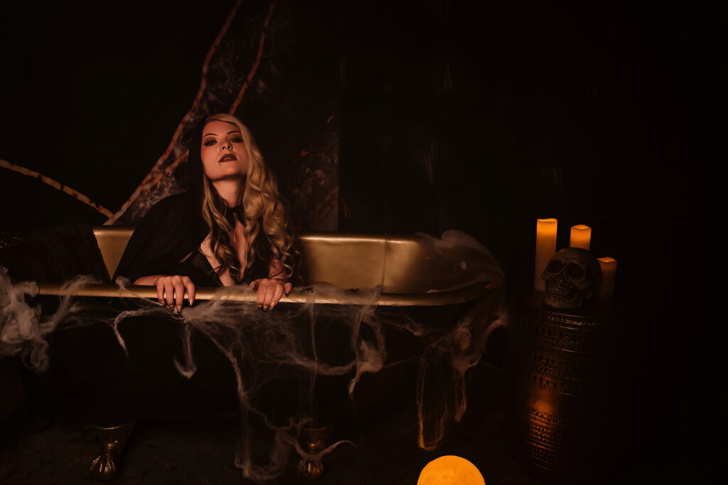 A woman sits in a black and gold claw foot tub inside a St. Louis area Boudoir Photo studio during their exclusive limited edition Spooky Boudoir Photo Sessions.