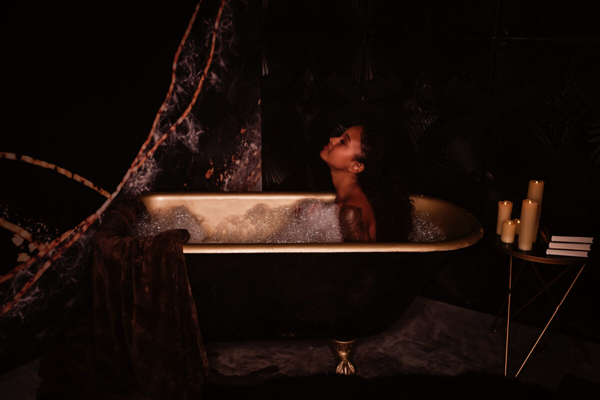 A woman with long dark hair sits in a black and gold claw foot tub full of bubbles, during her boudoir photography session with Love to the Moon Photography near St. Louis Missouri.