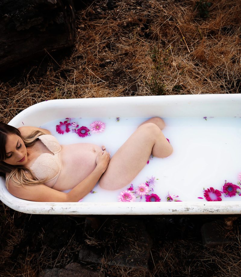Woman lays in outdoor bathtub for boudoir maternity photos also known as a milk bath.
