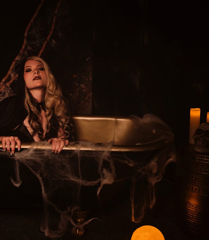 A woman sits in a black and gold claw foot tub inside a St. Louis area Boudoir Photo studio during their exclusive limited edition Spooky Boudoir Photo Sessions.