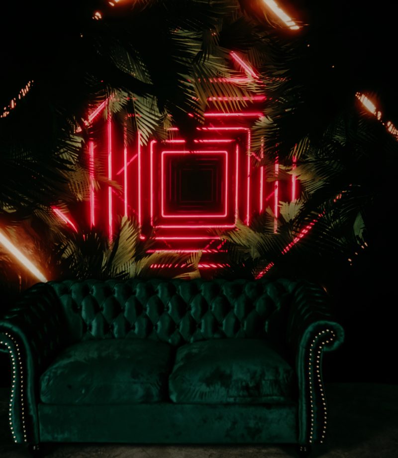 A neon sign with palm trees shines behind a velvet green sofa in a St. Louis Boudoir Photo Studio