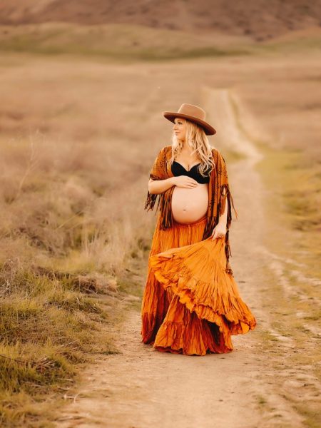A woman walks through a big empty field towards Photogrpaher Andrea Moore as she enjoys her maternity photo session.