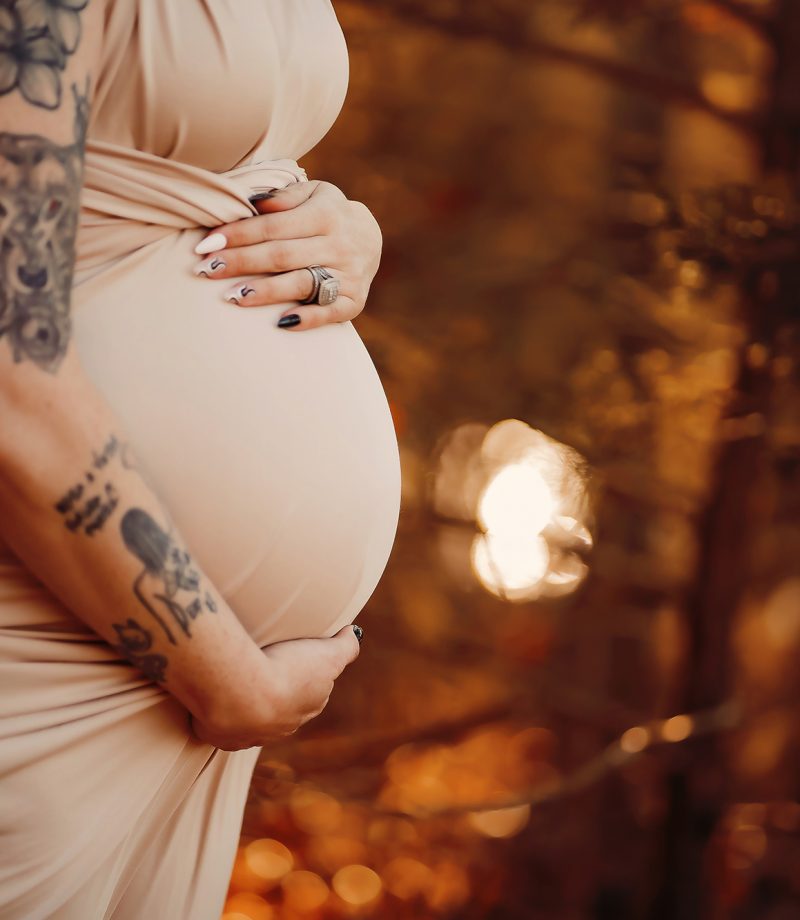 An up-close image of a pregnant belly in a beige form-fitting dress.